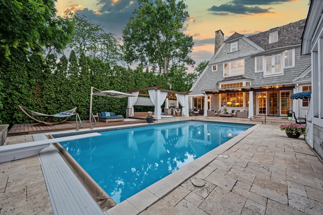 Swimming pool and stone terrace beside a warmly illuminated home at sunset